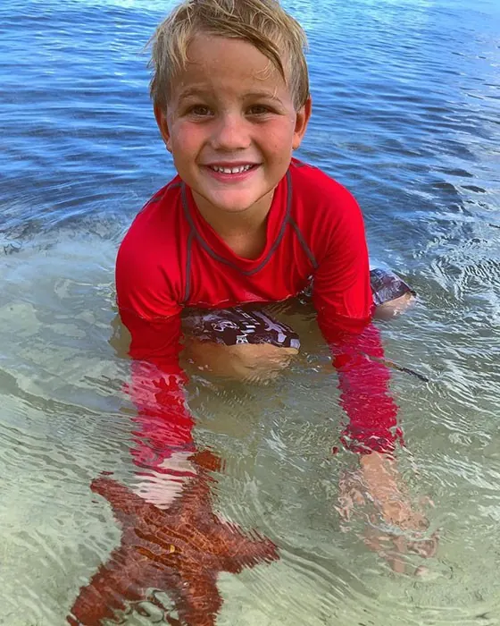 Boy with a red cushion sea star in the water at Starfish Point