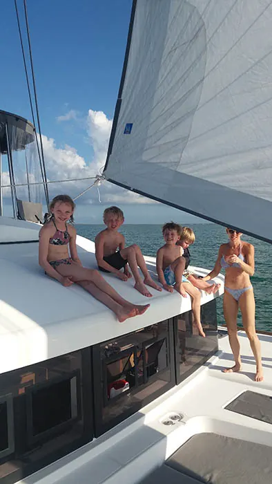 Children sitting on Bamboozled&rsquo;s deck under sail